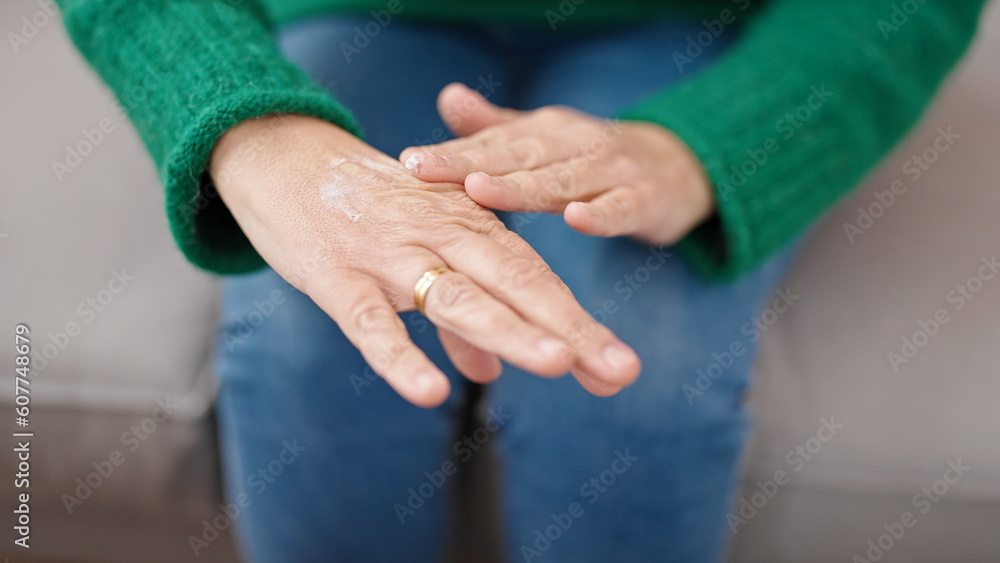 Mature hispanic woman with grey hair applying skin treatment sitting on sofa at home Mature hispanic woman with grey hair applying skin treatment sitting on sofa at home