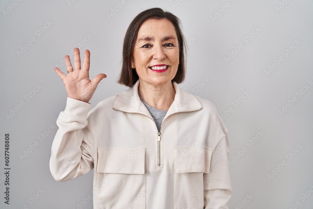 Middle age hispanic woman standing over isolated background showing and pointing up with fingers number five while smiling confident and happy. Middle age hispanic woman standing over isolated background showing and pointing up with fingers number five while smiling confident and happy.