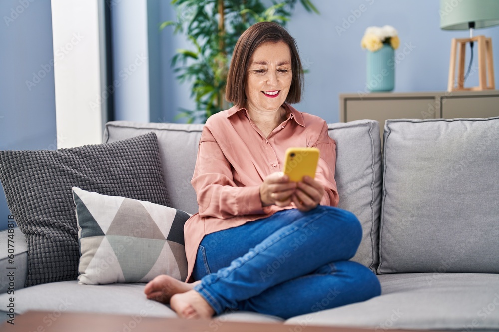Middle age woman using smartphone sitting on sofa at home Middle age woman using smartphone sitting on sofa at home