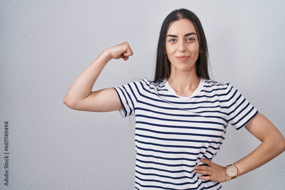 Young brunette woman wearing striped t shirt strong person showing arm muscle, confident and proud of power Young brunette woman wearing striped t shirt strong person showing arm muscle, confident and proud of power