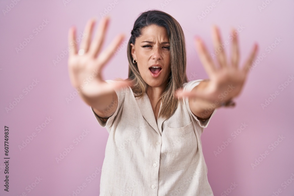 Blonde woman standing over pink background doing stop gesture with hands palms, angry and frustration expression Blonde woman standing over pink background doing stop gesture with hands palms, angry and frustration expression