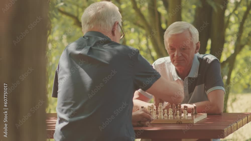 Waist up of two Caucasian mature men playing chess game outdoors in park on sunny day Waist up of two Caucasian mature men playing chess game outdoors in park on sunny day