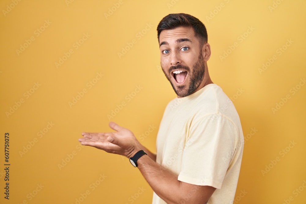 Handsome hispanic man standing over yellow background pointing aside with hands open palms showing copy space, presenting advertisement smiling excited happy Handsome hispanic man standing over yellow background pointing aside with hands open palms showing copy space, presenting advertisement smiling excited happy