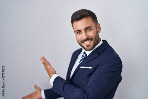 Handsome hispanic man wearing suit and tie inviting to enter smiling natural with open hand