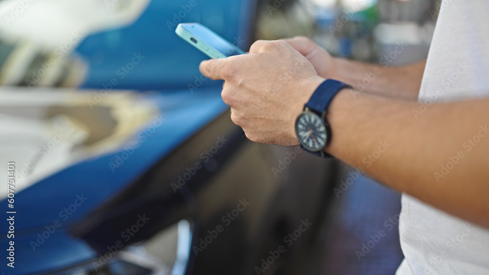 Young hispanic man using smartphone standing by car at street