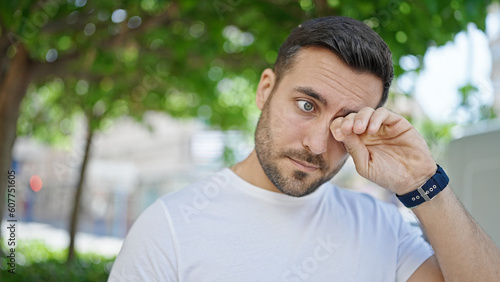 Young hispanic man standing with serious expression rubbing eyes at street photo
