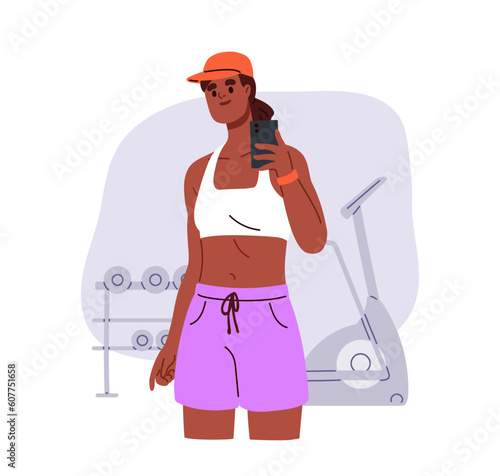 Woman takes photo on mobile phone in gym. Young slim girl and fitness selfie ...