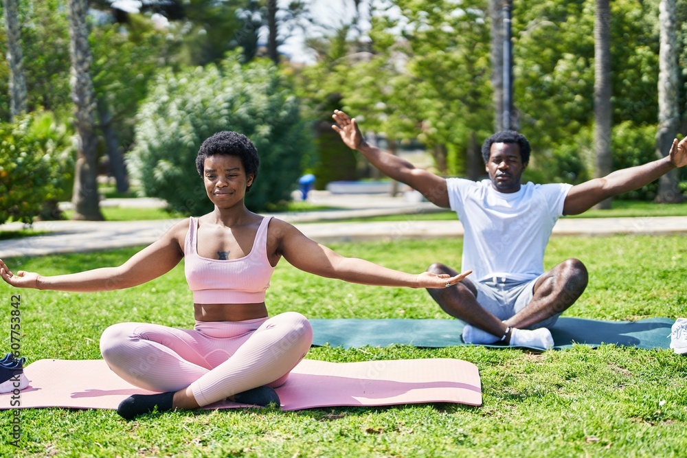 African american man and woman couple smiling confident doing yoga exercise at park African american man and woman couple smiling confident doing yoga exercise at park