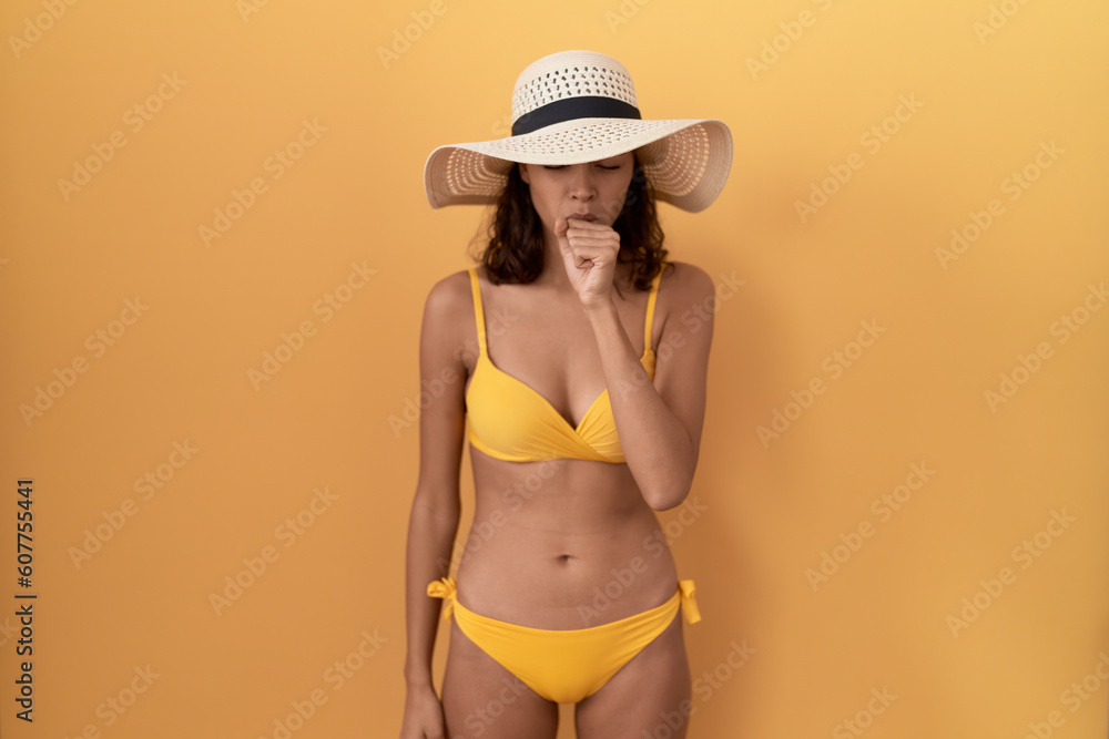 Young hispanic woman wearing bikini and summer hat feeling unwell and coughing as symptom for cold or bronchitis. health care concept. Young hispanic woman wearing bikini and summer hat feeling unwell and coughing as symptom for cold or bronchitis. health care concept.