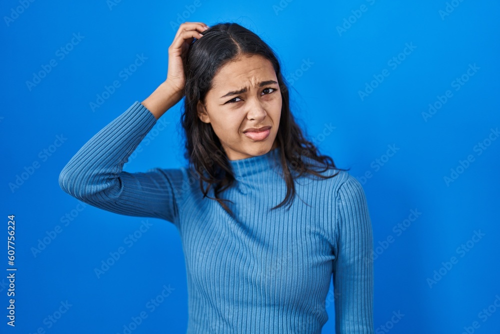 Young brazilian woman standing over blue isolated background confuse and wondering about question. uncertain with doubt, thinking with hand on head. pensive concept. Young brazilian woman standing over blue isolated background confuse and wondering about question. uncertain with doubt, thinking with hand on head. pensive concept.