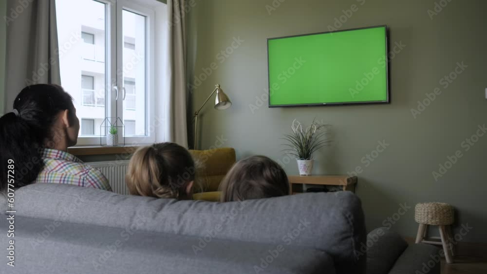 Family Sitting Together Sofa In Their Living Room Watching TV Green Screen. Rear View Of Family With Children Sitting On Sofa In Living Room Day Watching Green Mock-up Screen TV Together. Family Sitting Together Sofa In Their Living Room Watching TV Green Screen. Rear View Of Family With Children Sitting On Sofa In Living Room Day Watching Green Mock-up Screen TV Together.