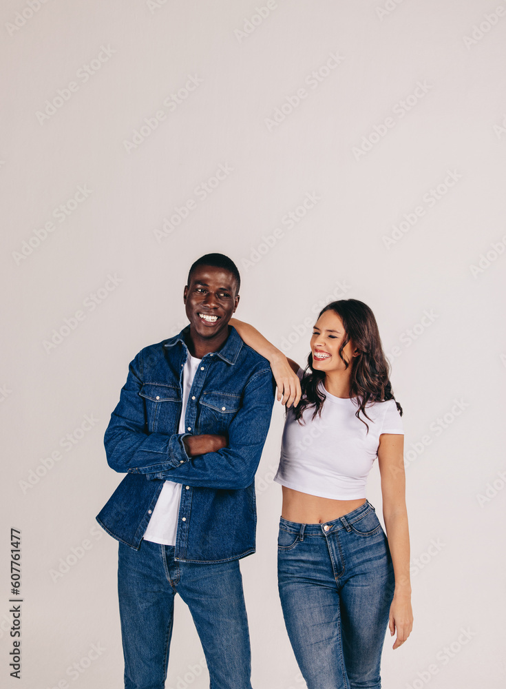 Denim-dressed couple smiles as they stand together in a studio setting Denim-dressed couple smiles as they stand together in a studio setting