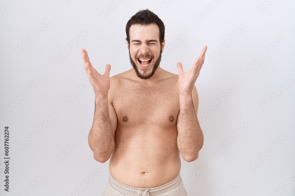 Fototapeta premium Young hispanic man standing shirtless over white background celebrating mad and crazy for success with arms raised and closed eyes screaming excited. winner concept