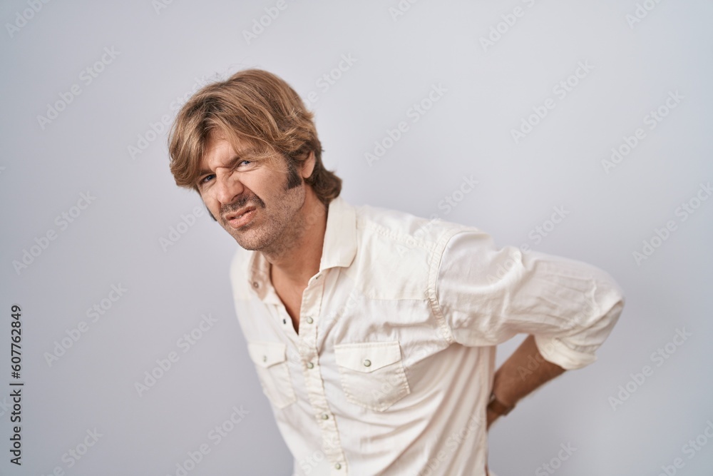 Middle age man standing over isolated background suffering of backache, touching back with hand, muscular pain Middle age man standing over isolated background suffering of backache, touching back with hand, muscular pain