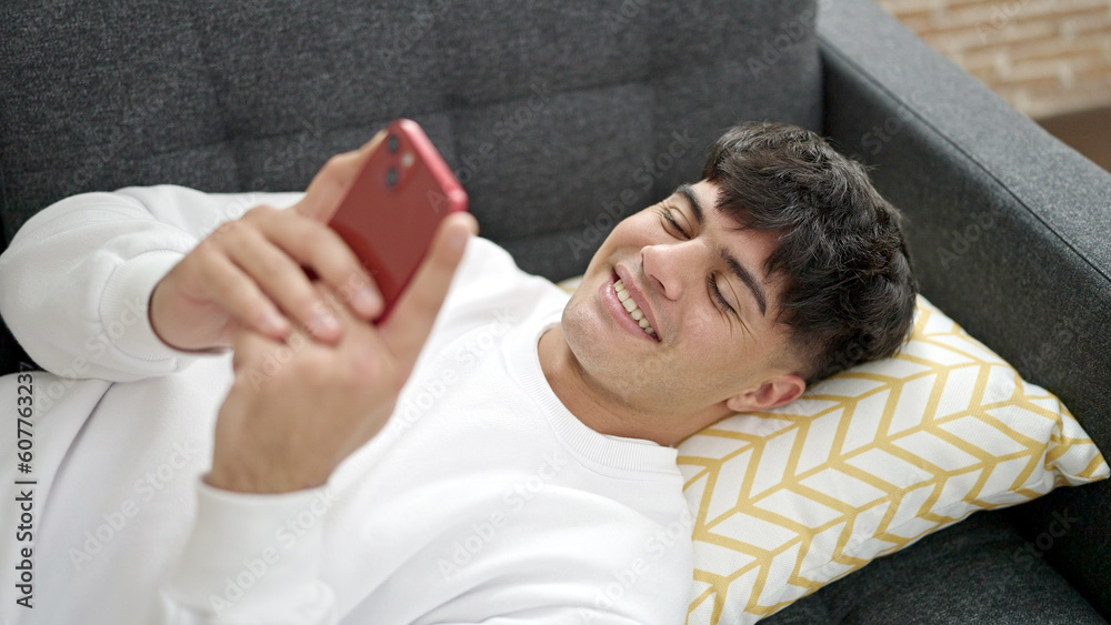 Obraz premium Young hispanic man using smartphone lying on sofa at home