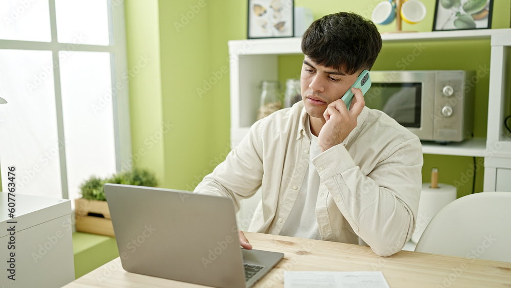 Young hispanic man using laptop talking on smartphone at dinning room Young hispanic man using laptop talking on smartphone at dinning room