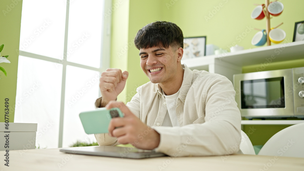 Young hispanic man playing video game sitting on table at dinning room