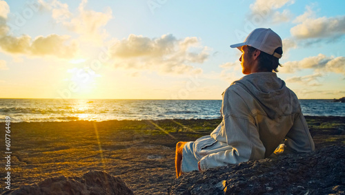 Man on a beach is looking distance during beautiful summer sunset. Human looks to the sun over horizon in the morning while sunrise. Happy person contemplates the beauty of nature. Freedom concept.