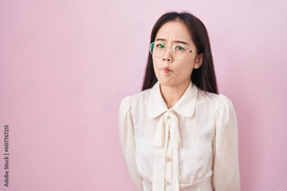 Young chinese woman standing over pink background making fish face with lips, crazy and comical gesture. funny expression.