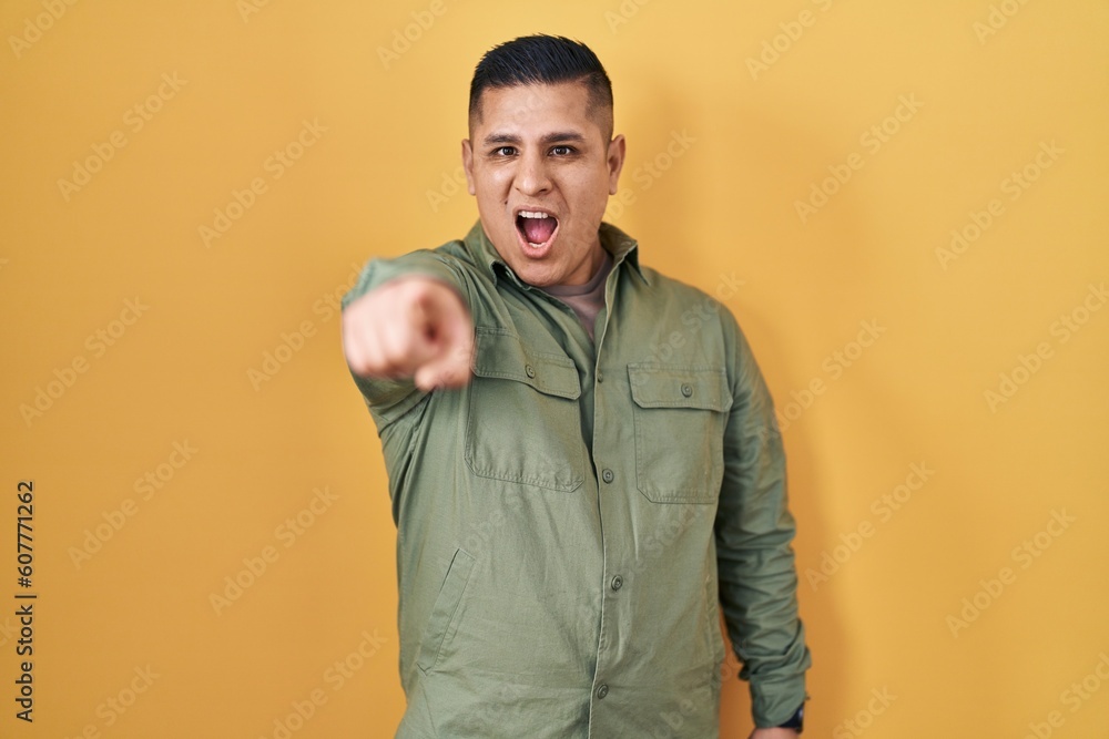 Hispanic young man standing over yellow background pointing displeased and frustrated to the camera, angry and furious with you Hispanic young man standing over yellow background pointing displeased and frustrated to the camera, angry and furious with you