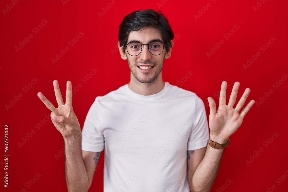 Naklejka premium Young hispanic man standing over red background showing and pointing up with fingers number eight while smiling confident and happy.