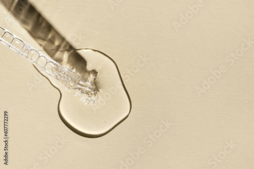 Facial serum with bubbles pouring from glass pipette on light yellow background. Transparent liquid gel or oil drop with collagen closeup. Beauty cosmetic product macro. Copy space, top view.