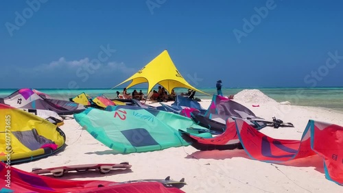 Kitesurfers preparing on coral sand cay beach with clear blue tropical water, colorful closeup