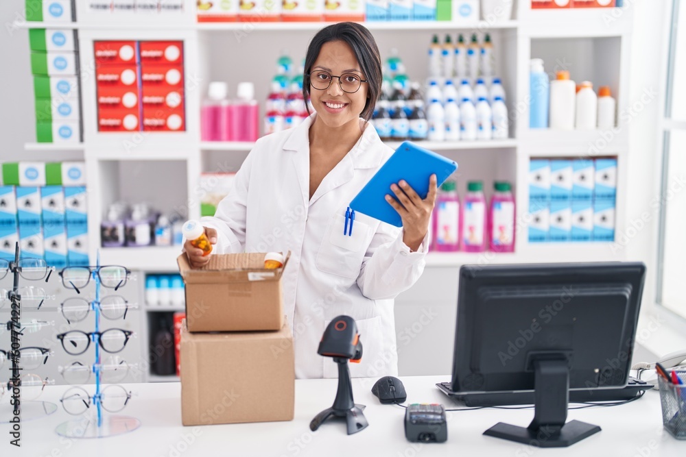 Young hispanic woman pharmacist using touchpad unboxing packages at pharmacy Young hispanic woman pharmacist using touchpad unboxing packages at pharmacy