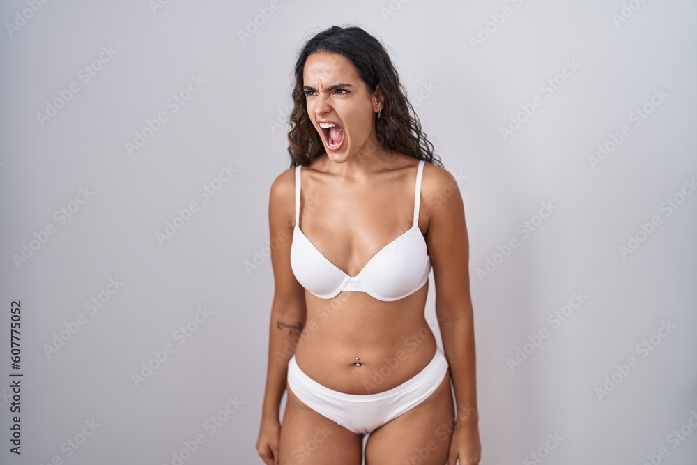 Obraz premium Young hispanic woman wearing white lingerie angry and mad screaming frustrated and furious, shouting with anger. rage and aggressive concept.