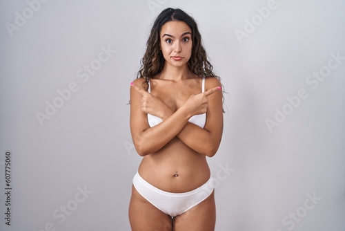 Young hispanic woman wearing white lingerie pointing to both sides with fingers, different direction disagree