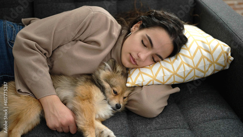 Young hispanic woman with dog lying on sofa sleeping together at home