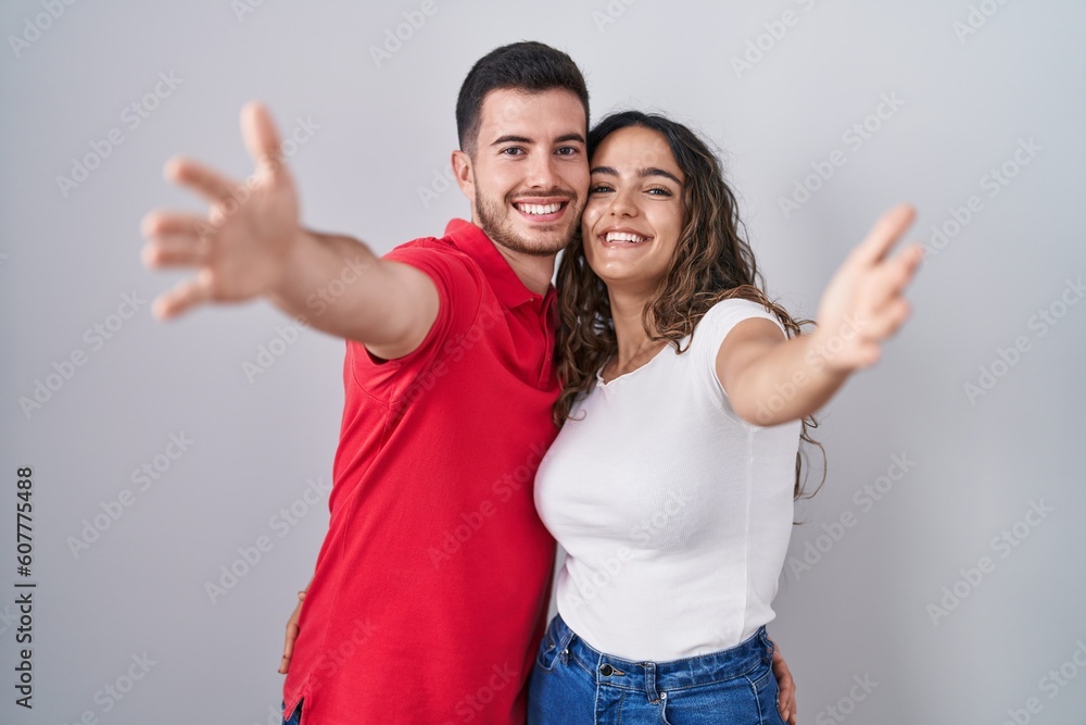 Young hispanic couple standing over isolated background looking at the camera smiling with open arms for hug. cheerful expression embracing happiness. Young hispanic couple standing over isolated background looking at the camera smiling with open arms for hug. cheerful expression embracing happiness.