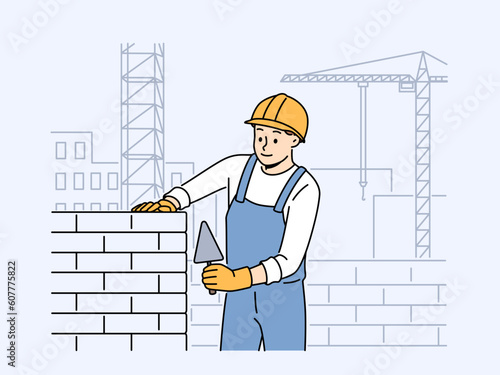 Positive male worker in uniform and helmet building house with bricks. Smiling man engineer busy laying blocks at construction site. Vector illustration. 