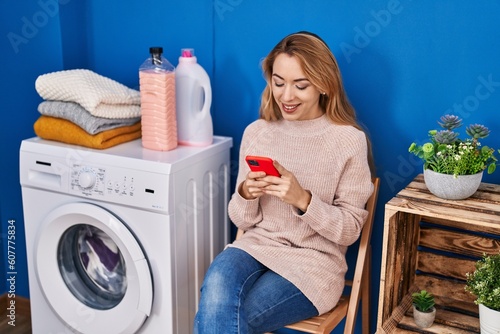 Young woman using smartphone waiting for washing machine at laundry room