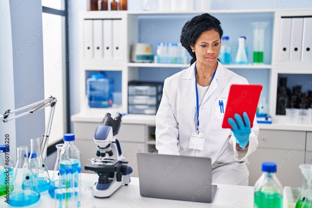 African american woman wearing scientist uniform using touchpad at laboratory African american woman wearing scientist uniform using touchpad at laboratory