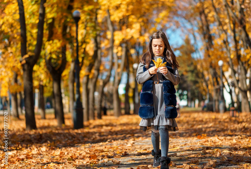 the girl is walking in the autumn city park, she is happy and enjoys the beautiful nature, holding yellow maple leaves in her hands, a bright sunny day © soleg