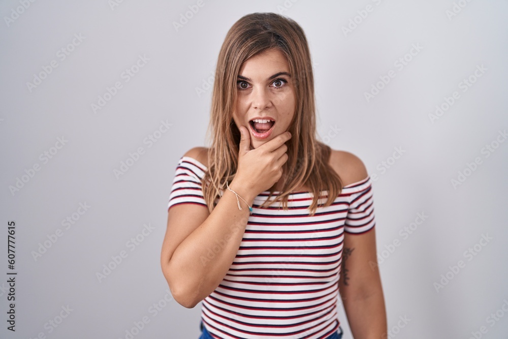 Young hispanic woman standing over isolated background looking fascinated with disbelief, surprise and amazed expression with hands on chin Young hispanic woman standing over isolated background looking fascinated with disbelief, surprise and amazed expression with hands on chin