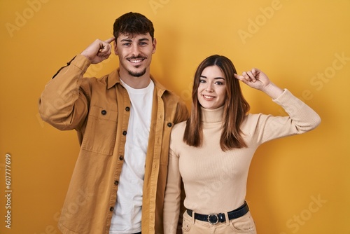 Young hispanic couple standing over yellow background smiling pointing to head with one finger, great idea or thought, good memory
