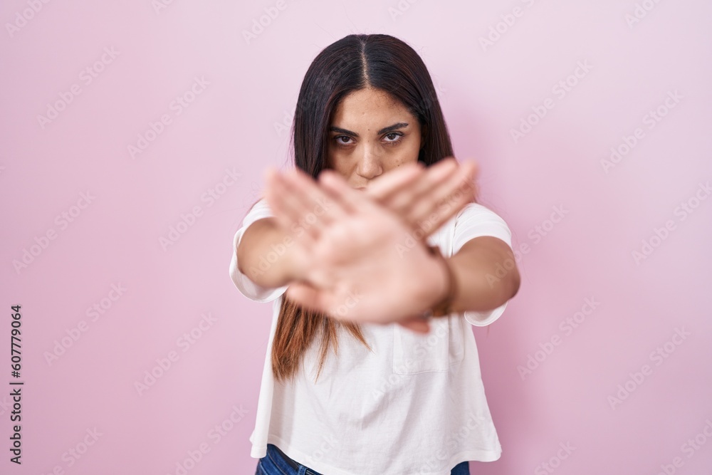 Young arab woman standing over pink background rejection expression crossing arms and palms doing negative sign, angry face Young arab woman standing over pink background rejection expression crossing arms and palms doing negative sign, angry face