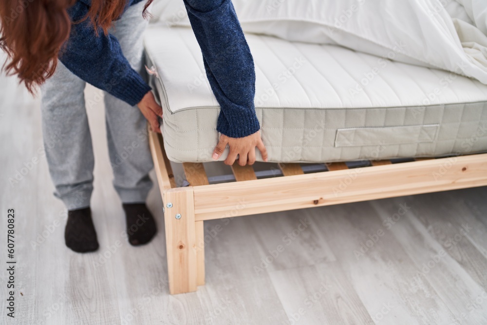Fototapeta premium Young hispanic woman holding mattress bed at bedroom