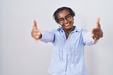 African woman with dreadlocks standing over white background wearing glasses looking at the camera smiling with open arms for hug. cheerful expression embracing happiness.