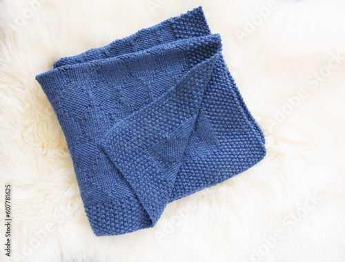 Navy blue wool knitted blanket in harlequin knitting pattern on a white furry background