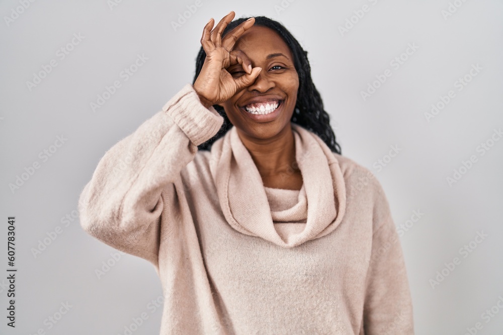African woman standing over white background doing ok gesture with hand smiling, eye looking through fingers with happy face. African woman standing over white background doing ok gesture with hand smiling, eye looking through fingers with happy face.