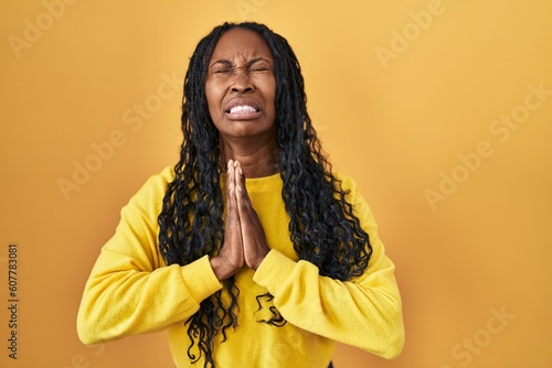 African woman standing over yellow background begging and praying with hands together with hope expression on face very emotional and worried. begging.