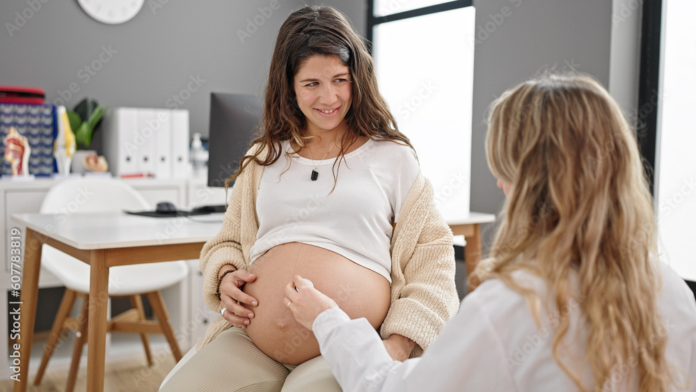 Obraz premium Young pregnant woman gynecologist and patient examining belly with stethoscope at clinic