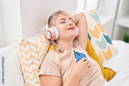 Young blonde woman listening to music relaxed on bed at bedroom