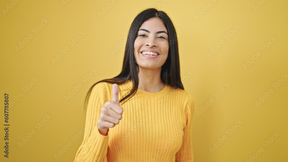 Young beautiful hispanic woman smiling with thumb up over isolated yellow background Young beautiful hispanic woman smiling with thumb up over isolated yellow background