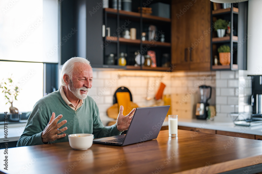 Close up of a senior man using a laptop in the kitchen. Shot of a senior man sitting alone and using his laptop to calculate his finances at home. Portrait of senior man using laptop at home Close up of a senior man using a laptop in the kitchen. Shot of a senior man sitting alone and using his laptop to calculate his finances at home. Portrait of senior man using laptop at home