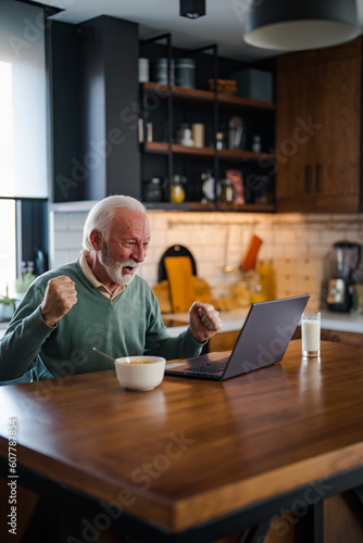 Happy excited old elderly man winner excited by reading good news looking at laptop, overjoyed senior mature grandfather watching game online celebrating goal bid bet win great result victory concept © Dragana Gordic