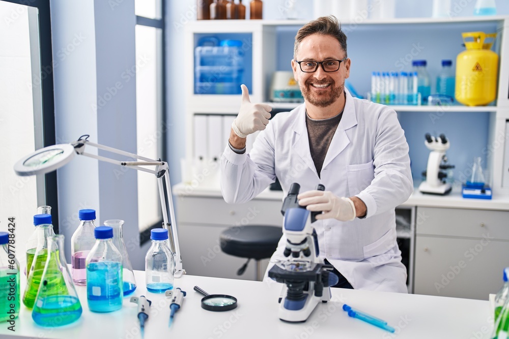 Middle age caucasian man working at scientist laboratory smiling happy and positive, thumb up doing excellent and approval sign